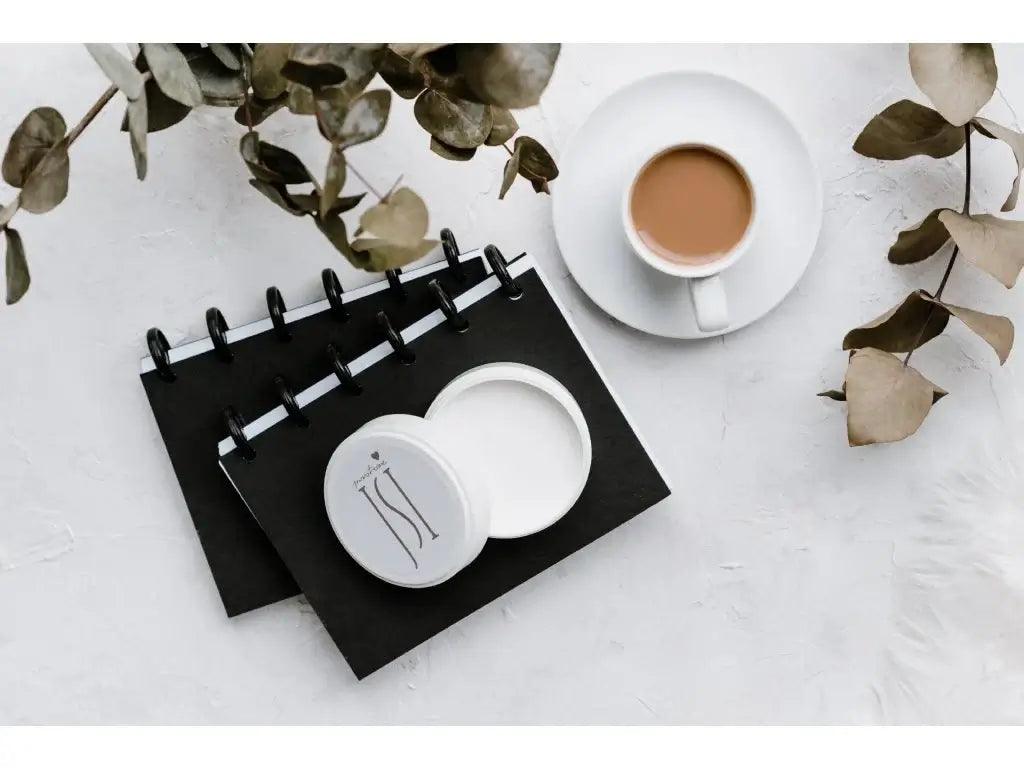 Stylizovaný stůl s černými zápisníky, šálkem kávy a kosmetickým produktem, ideální pro relaxaci a inspiraci.