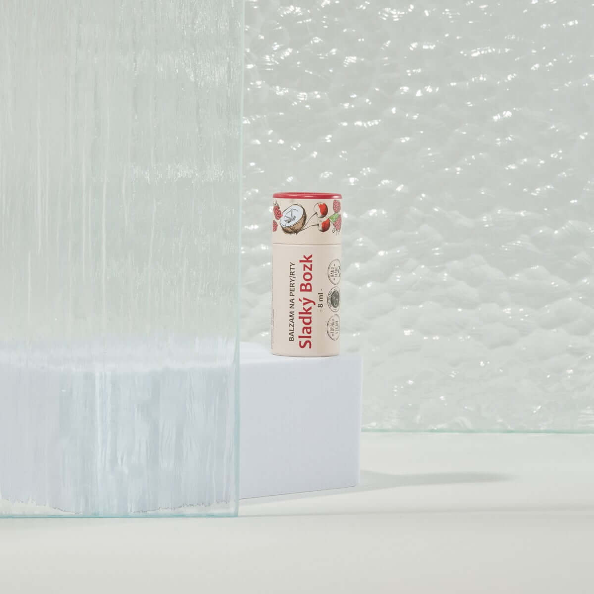 Kvitok Balzám Na Rty Sladký Polibek 8 ml mezi skleněnými povrchy, ideální pro hydrataci a ochranu rtů.